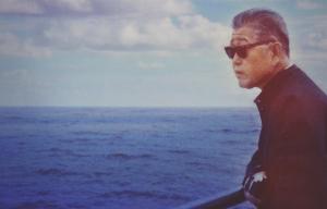 95 and 6 to Go poster. A middle-aged Japanese man in sunglasses stands at a ship's railing and looks out over a vast, dark blue sea.